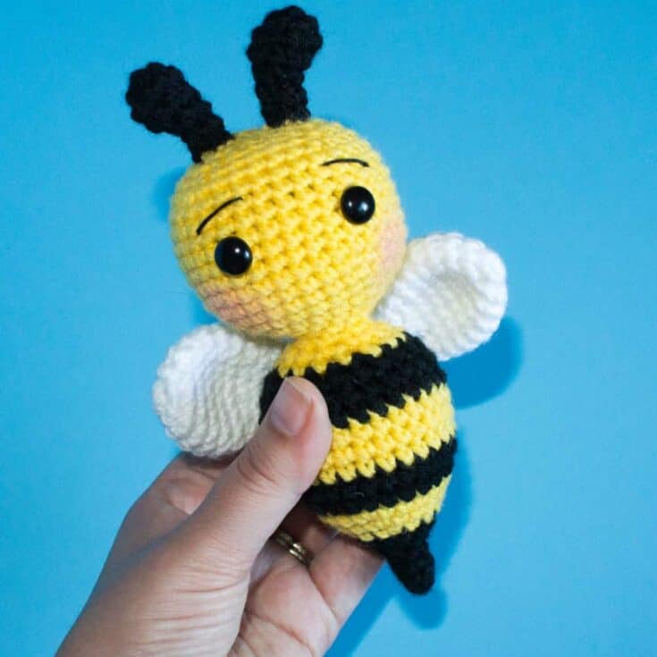 A person displaying a handmade crochet bee amigurumi.