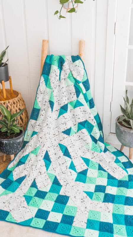 A granny square blanket on a chair next to a potted plant.