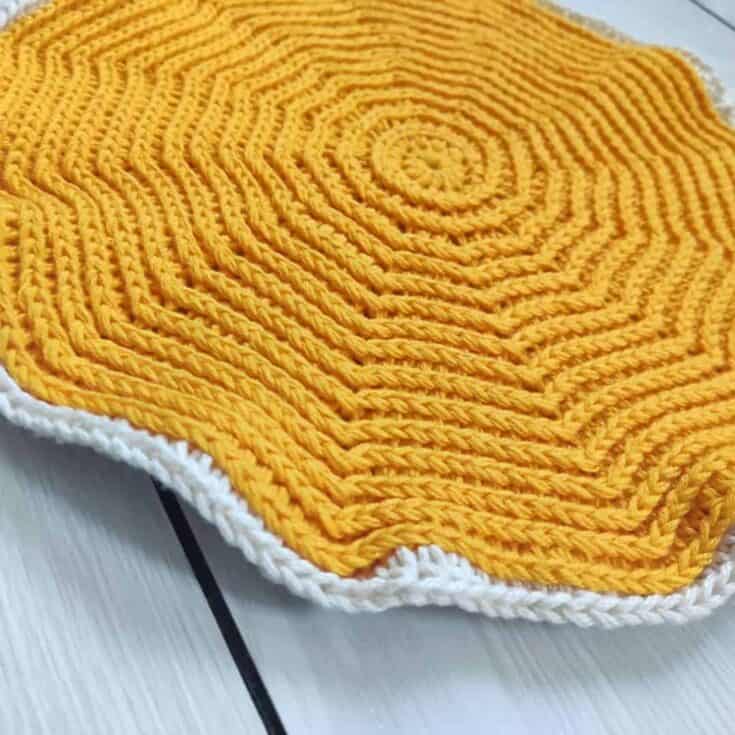 A yellow crocheted dishcloth on a wooden table.