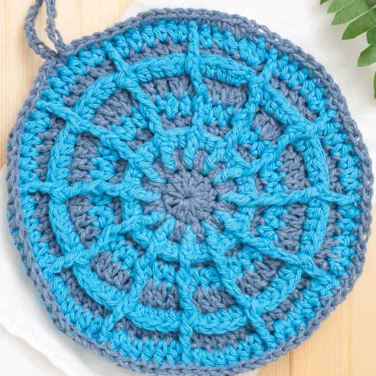 A blue and gray crocheted pot holder on a wooden table.