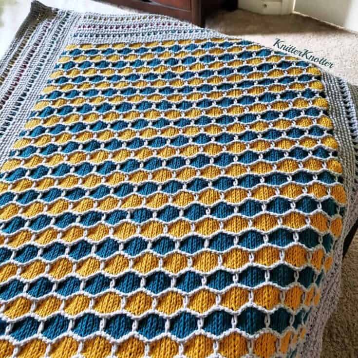 A yellow and blue crocheted afghan on a bed.