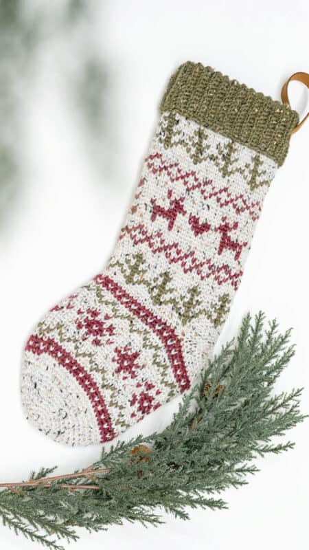 A knitted Christmas stocking, crafted with a crochet stocking pattern, hanging on a branch.