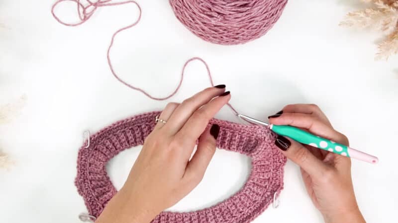 A pair of hands with dark painted nails holding yarn and a crochet hook. 