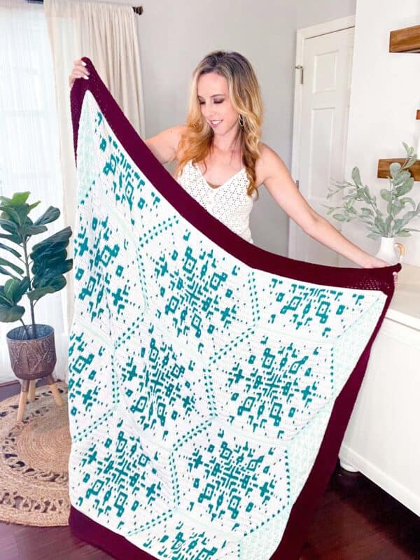 A woman is showcasing a crochet blanket with a snowflake pattern.