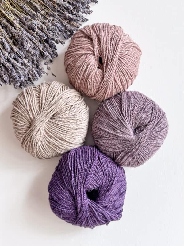 Four balls of yarn next to a bunch of lavender flowers, perfect for crochet.