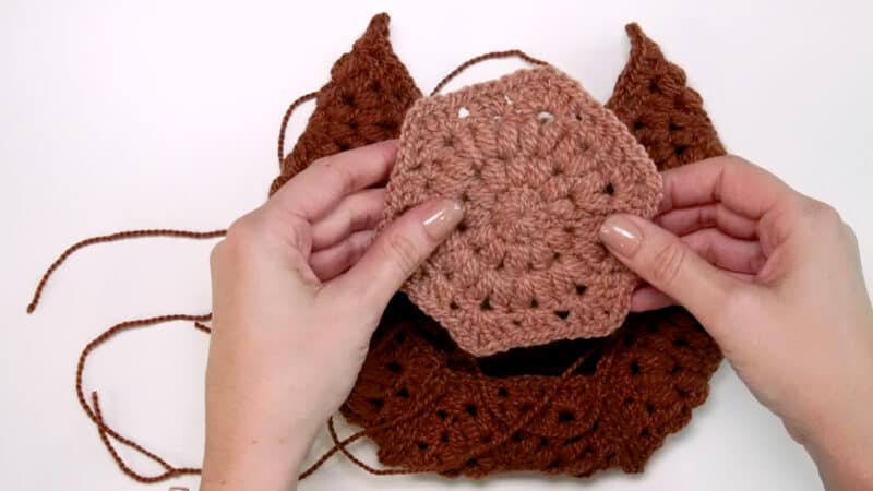 Hands holding a crochet hexagon square placing it on top of others.