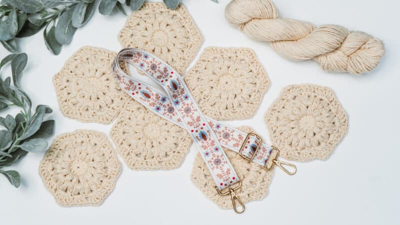 A crocheted hexagon with lanyard with yarn and flowers.