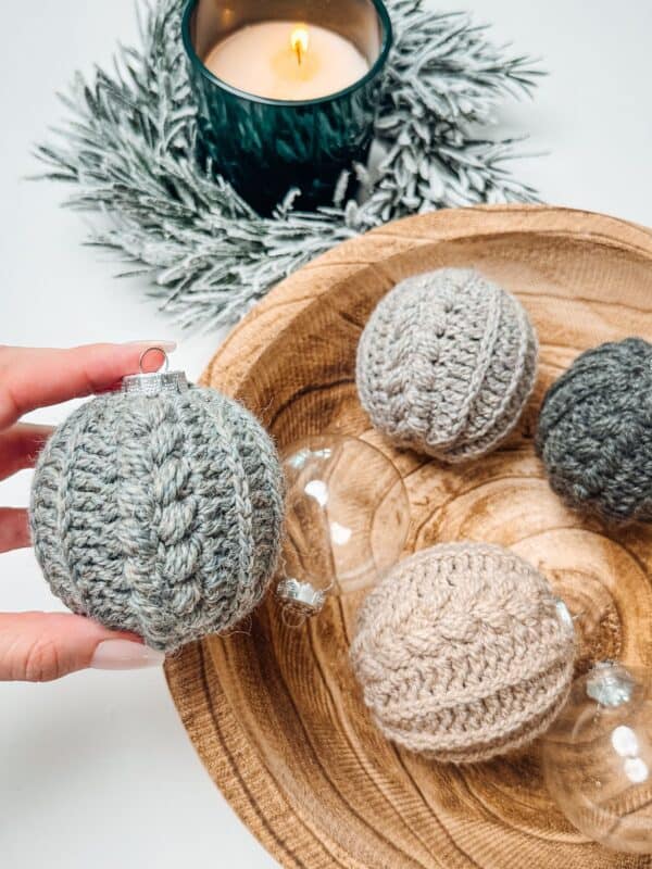 Crocheted Christmas ornaments on a wooden plate, featuring a unique crochet sweater pattern.