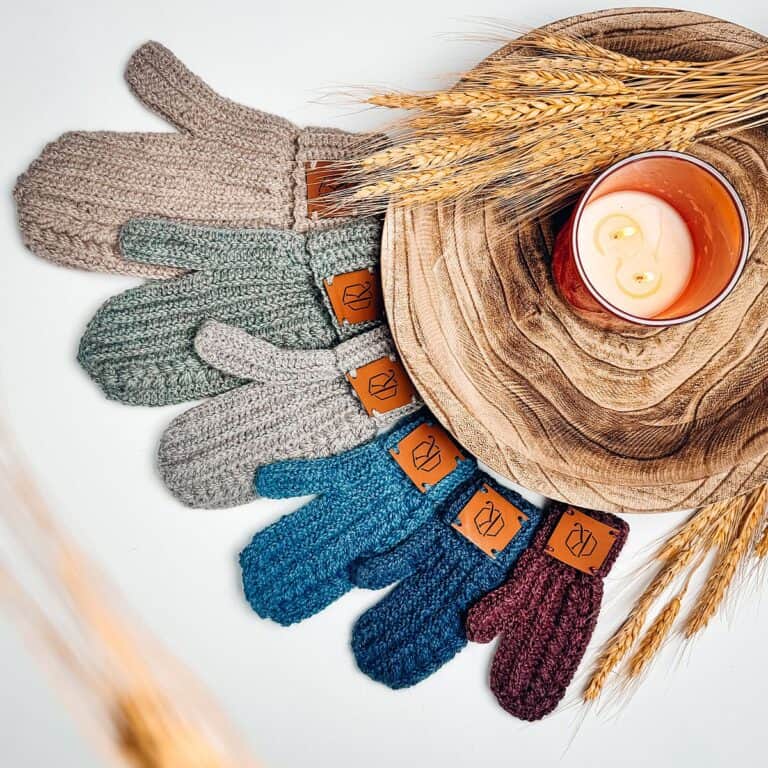 Knitted mittens on a wooden plate with a crochet sweater pattern.