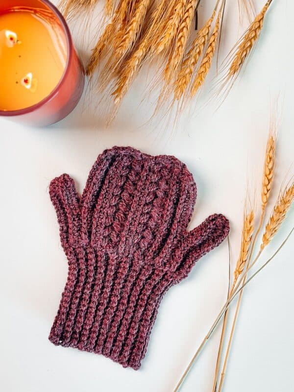 A crochet mitten with a candle and wheat.