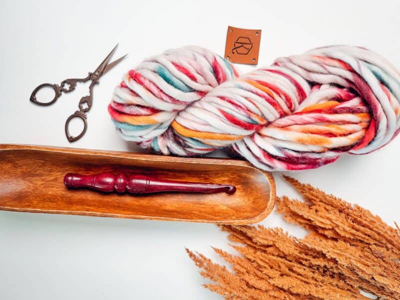 Skeins of yarn and scissors on a wooden table, perfect for your crochet sweater pattern.