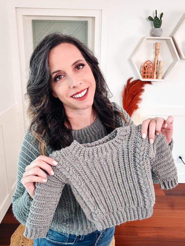 A woman showcasing a gray knitted baby sweater.
