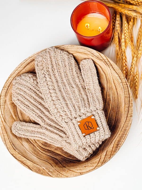 Crochet mittens delicately placed on a wooden plate alongside a flickering candle.