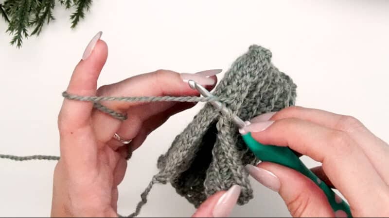 A person knitting a scarf with a pair of crochet.