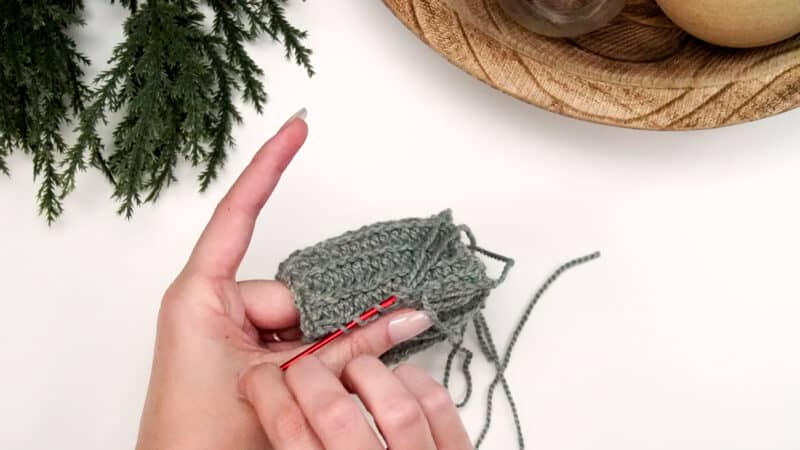 A person is holding a crocheted ball in front of a Christmas tree, showcasing their crochet skills.