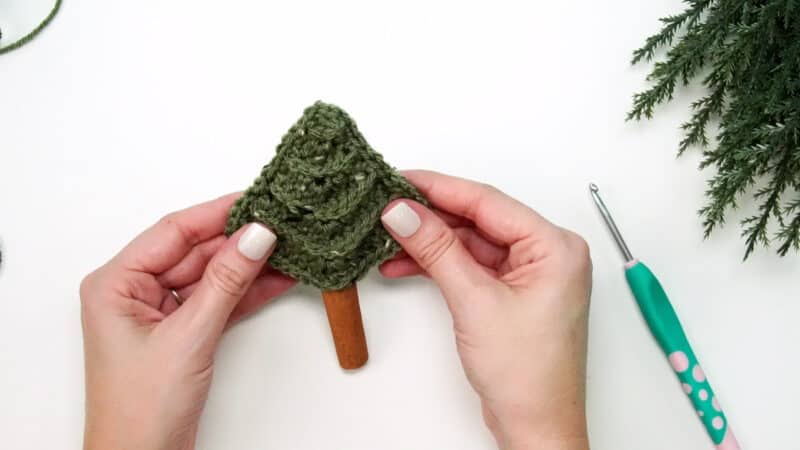 A person is holding a crocheted Christmas tree, as part of their Crochet Advent Calendar.