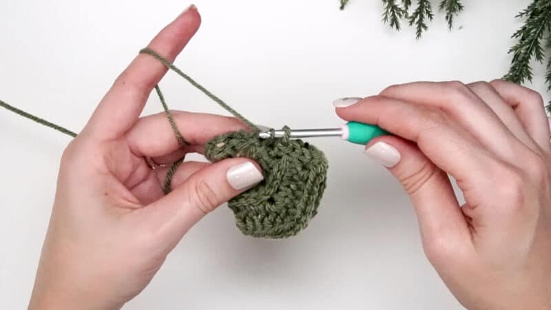A person is crocheting two green pieces together.