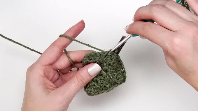 A person is using a crochet hook to make a green crocheted ball, ignoring the keywords "Child Sweater".
