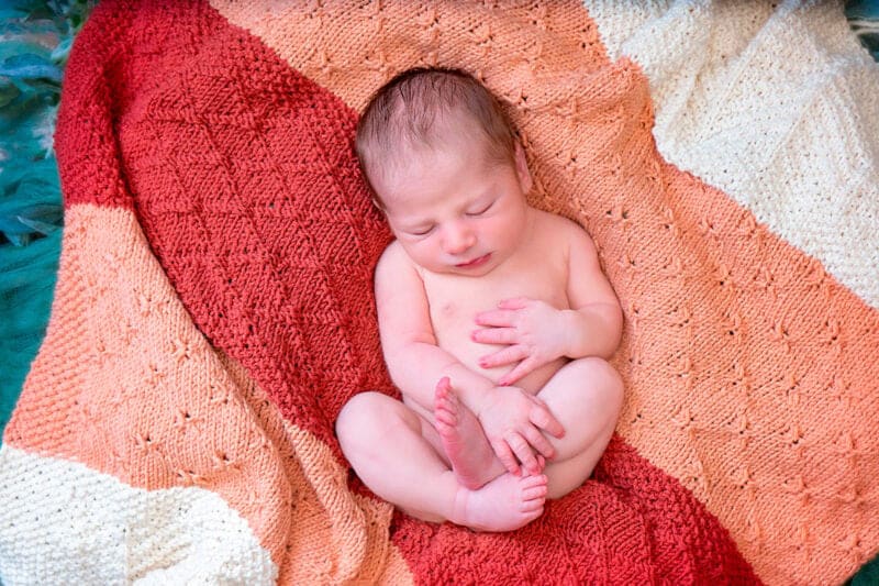 A baby sleeping in a red and orange blanket.