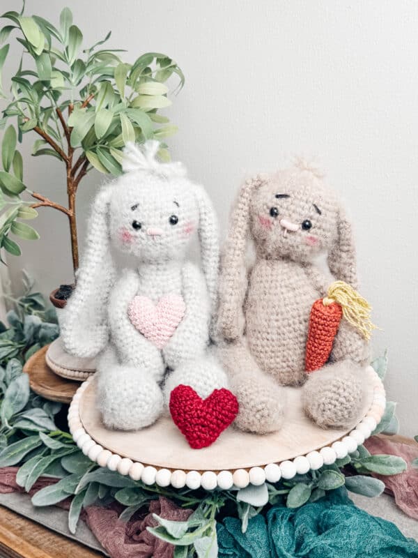 Two crocheted bunnies sitting on a plate with carrots wearing crochet granny square cardigans.