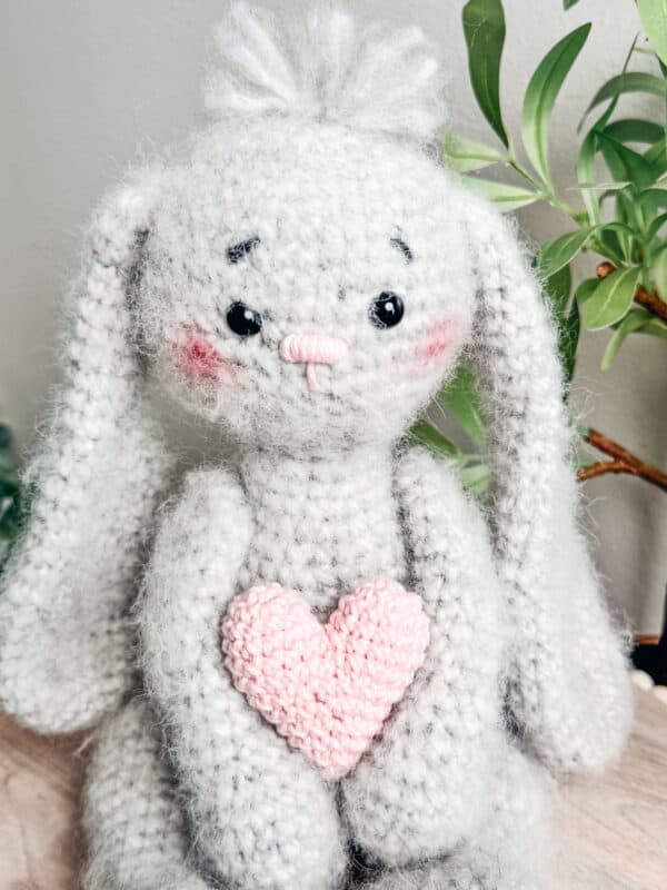 A grey crochet bunny holding a pink heart.