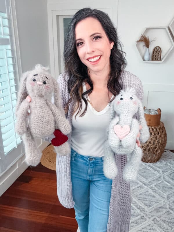 A woman wearing a Crochet Granny Square Cardigan holds two stuffed animals in her living room.