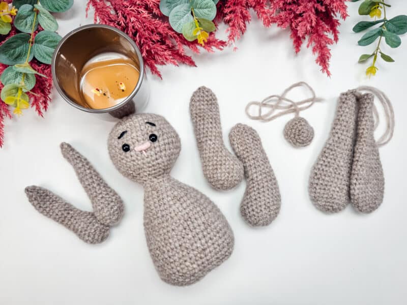 A crocheted bunny sitting next to a cup of coffee wearing a crochet granny square cardigan.