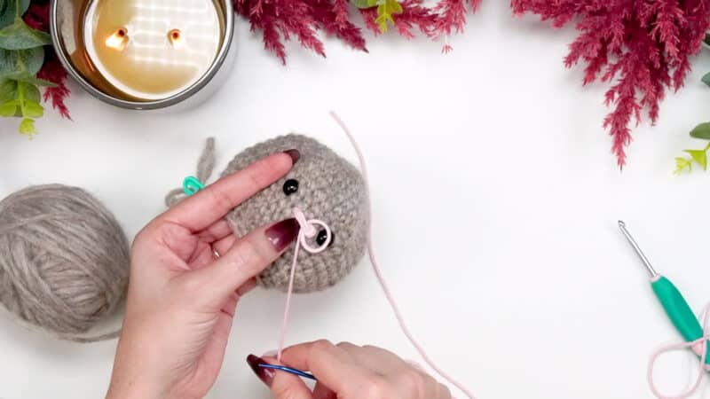 A person is knitting a granny square stuffed animal with yarn.