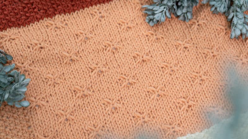 A close up of a knitted blanket with pine needles.