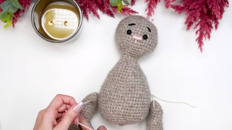 A person crocheting a stuffed animal while wearing a granny square cardigan.