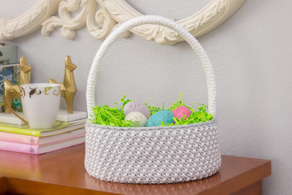 A white basket with easter eggs sits on top of a dresser.