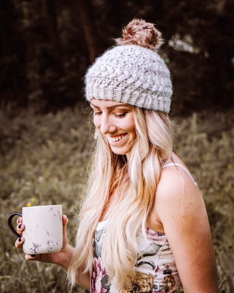A blonde woman holding a coffee mug in a field.