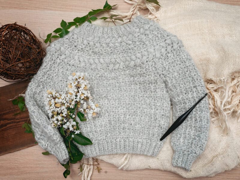 A sweater with flowers and a pen on a wooden table.