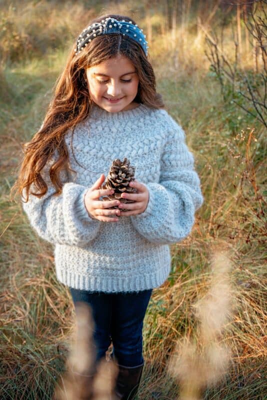 A little girl holding a pine cone in a field.