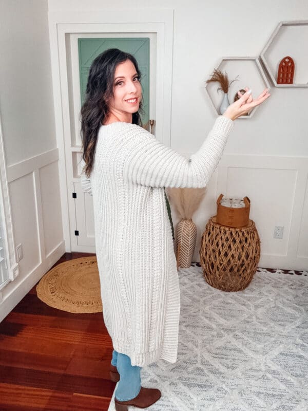 A woman standing in a living room wearing a cardigan.