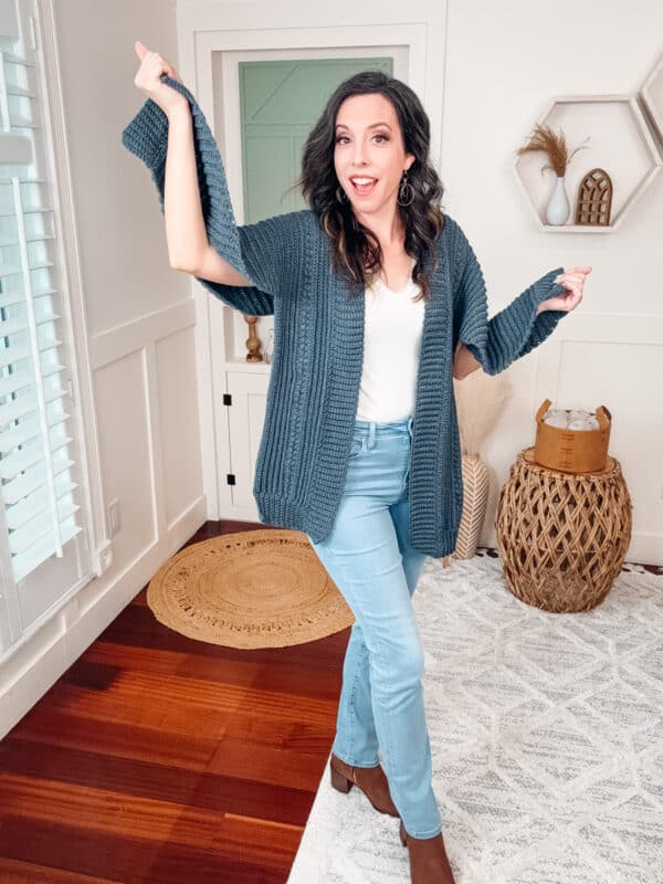 A woman wearing jeans and a cardigan in a living room.