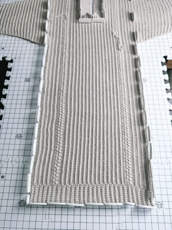 A crochet sweater on a blocking mat with pins.