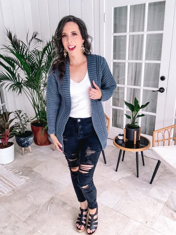 A woman wearing ripped jeans and a cardigan.