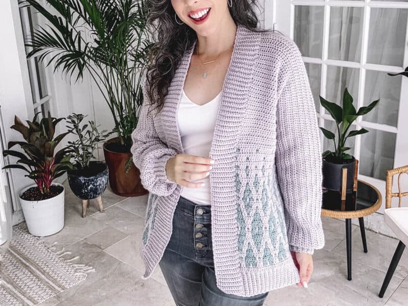 Woman smiling and posing in a casual outfit with a hand-knit cardigan from the Autumn Wheat Crochet Collection.