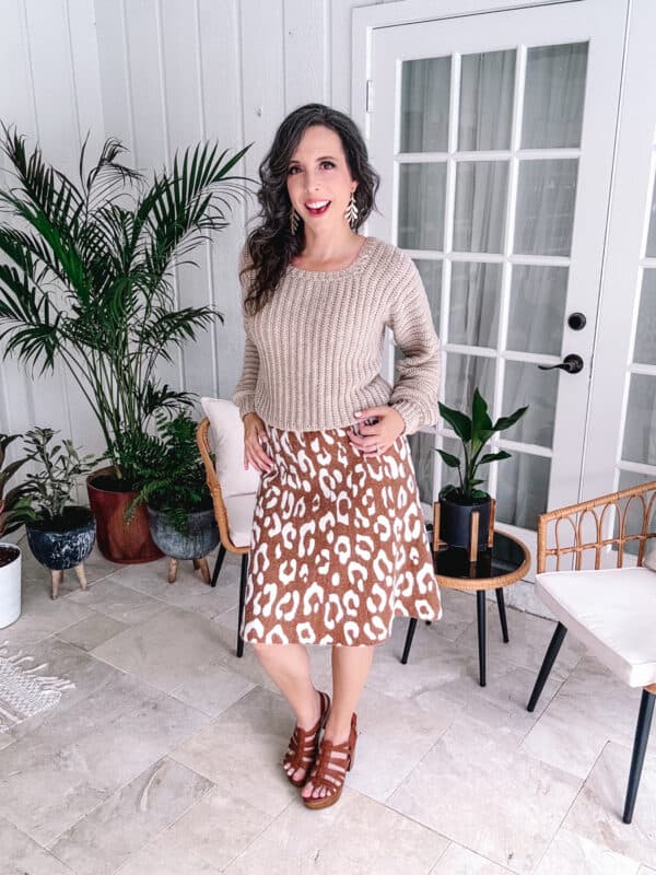 Woman standing in a room wearing an Autumn Wheat crochet sweater and animal print skirt.