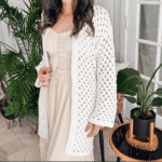 Woman wearing an easy crochet cardigan in white over a cream dress. Text overlay reads: Regency Flat Crochet Cardigan in 9 sizes.