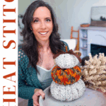 Woman sitting at a table with three stacked crochet pumpkins, a crochet doily, and dried flowers; text reads “Wheat Stitch Pumpkins” and “Pumpkin Spice Crochet Pumpkin Trio Pattern + Free Video Tutorial.”.