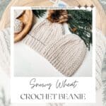 Crochet beanie with a pom-pom, artfully placed on a wooden tray amidst greenery. The text reads "Snowy Wheat Puff Crochet Hat Pattern" and "Free Pattern + Video Tutorial.