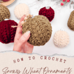 Hand holding a crocheted ornament among other ornaments, with hot tea and a branch in the background. Text overlay reads: "How to Crochet Snowy Wheat Ornaments, Free Crochet Pattern + Video Tutorial.