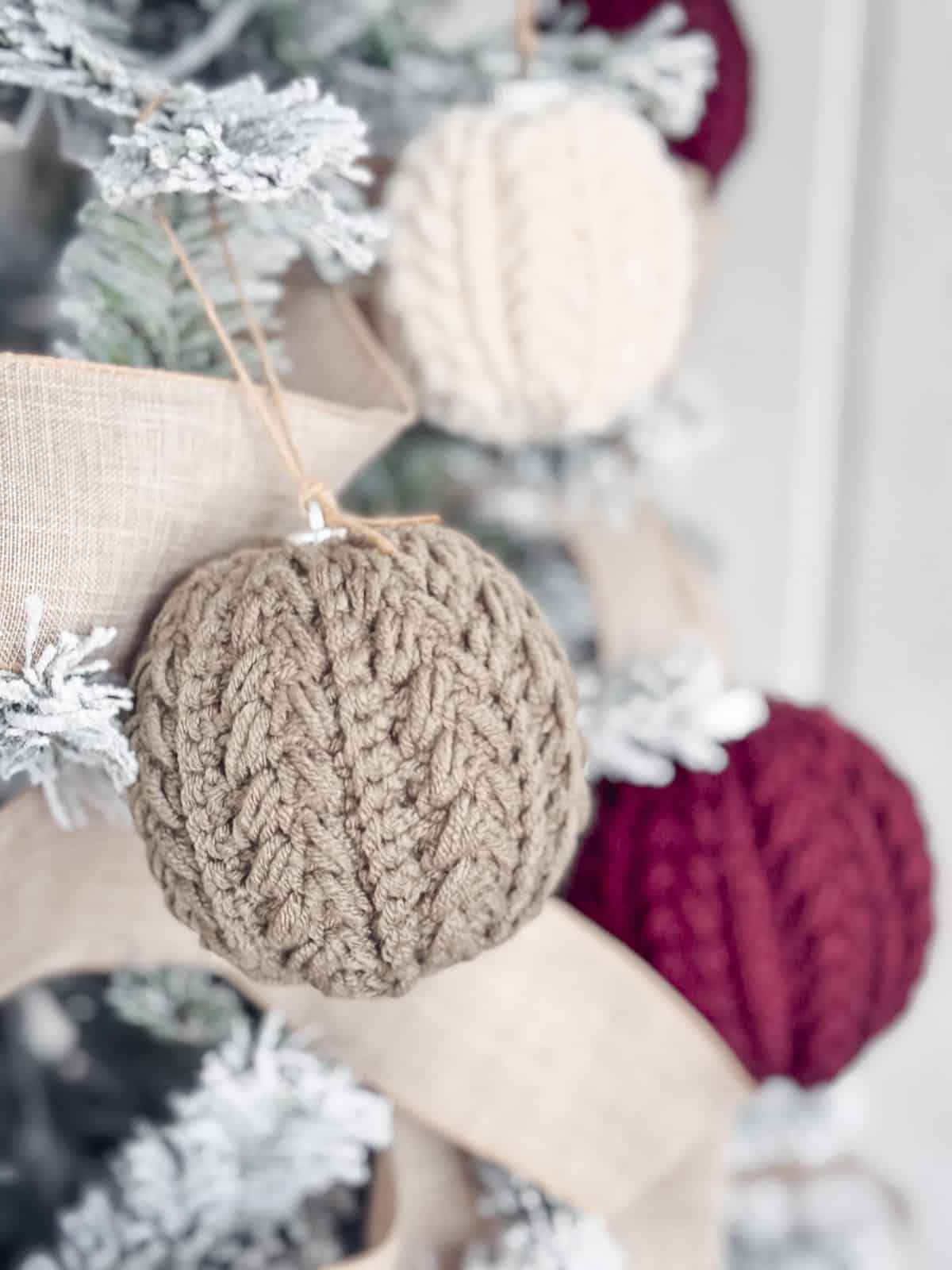 Close-up of a Christmas tree decorated with knitted ornaments in beige, red, and cream colors.