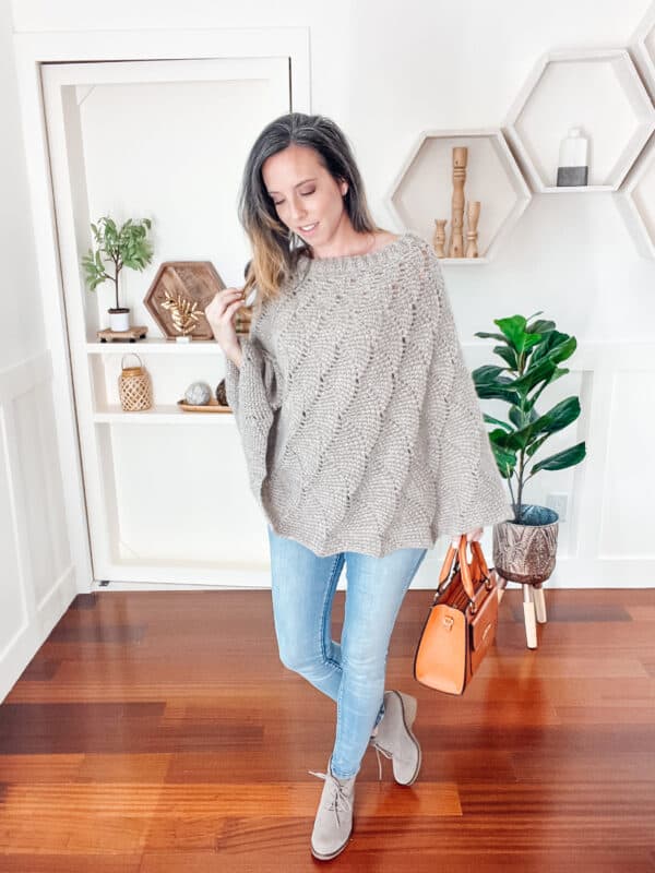 Woman in a cozy knit sweater and jeans stands in a modern room with hexagonal shelves and plants.