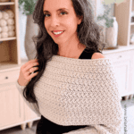 Woman wearing a handmade Winter Wheat Crochet Sweater Scarf Pattern, standing in a cozy room with yarn and decor in the background. Text overlay reads, “How to Crochet a Wheat Stitch Sweater Scarf.”.