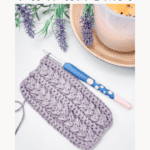 Crochet sample and hook on a table with lavender and a candle. Text: "How to Crochet The Wheat Stitch - Step-by-Step Written Instructions + Video Tutorial.