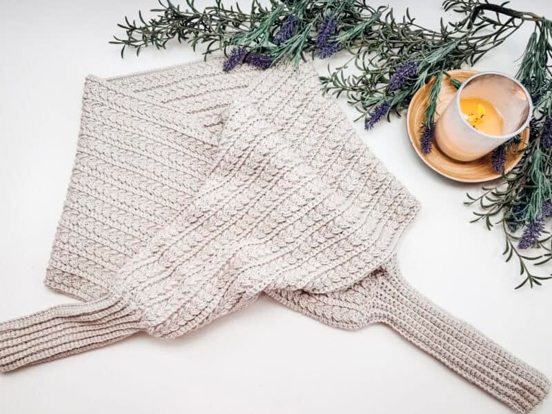 A cream-colored knitted sweater lies on a white surface with lavender sprigs and a lit candle in a small dish nearby.