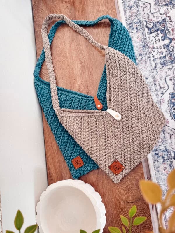 Two knitted bags, one teal and one beige, with leather tags and handles, are placed on a wooden surface beside a white bowl and green plant—perfect inspo for your next Wheat Stitch Crochet Rectangle Bag Pattern project.